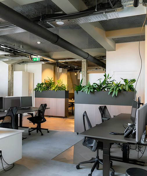 Open-plan office workspace interior in Dubai, featuring modern workstations with ergonomic chairs, integrated planters with greenery, and an industrial ceiling design with exposed ducts.